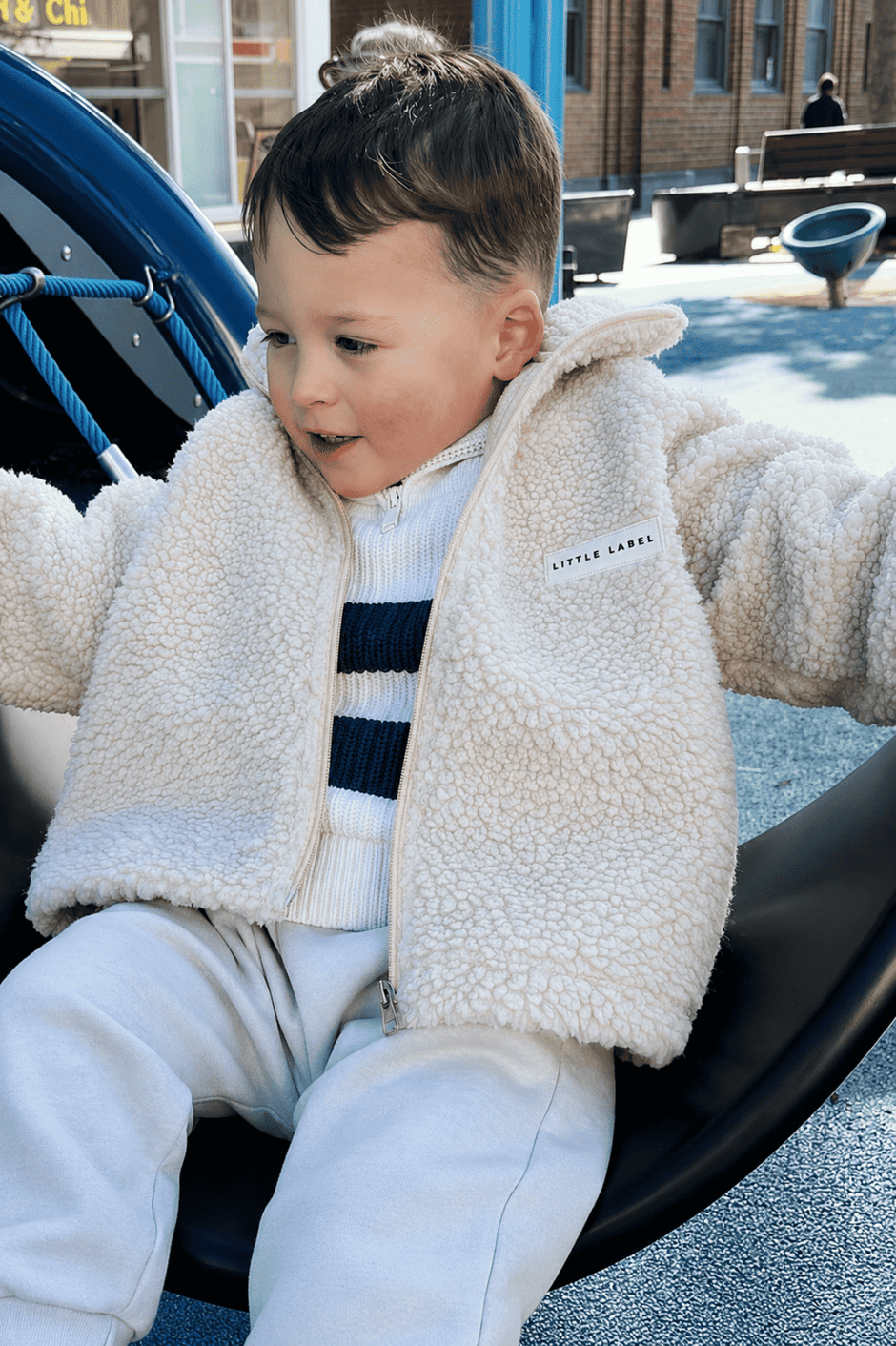 Child wearing a beige fleece jacket sitting on playground equipment