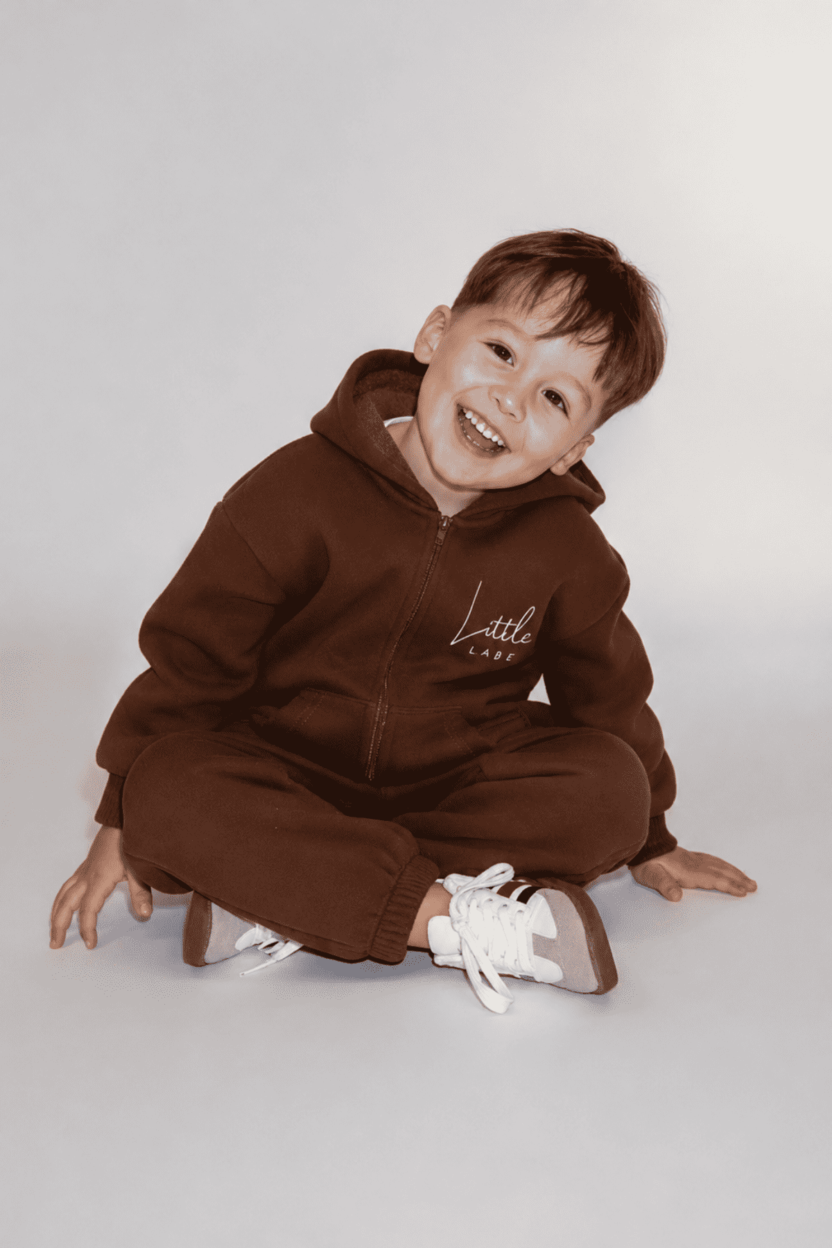 Child wearing a brown hoodie and pants sitting on a white background | Ryan is 3'3
