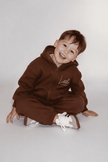 Child wearing a brown hoodie and pants sitting on a white background | Ryan is 3'3