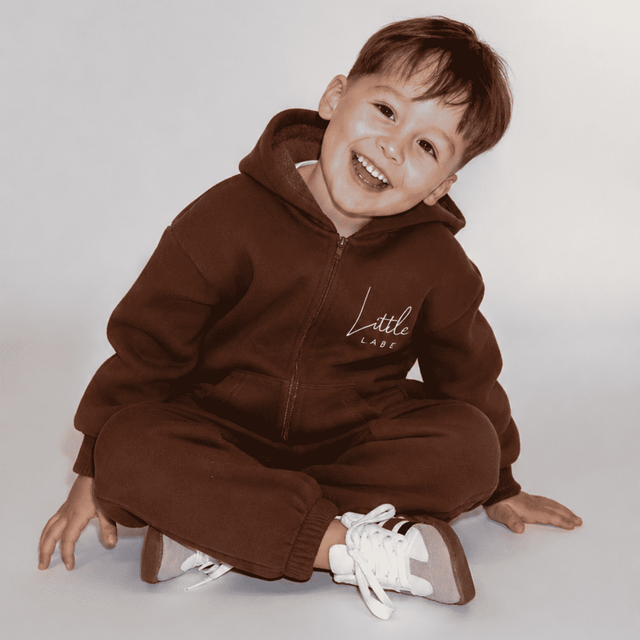 Child wearing a brown hoodie and pants sitting on a white background | Ryan is 3'3" (100cm), wears size 3Y