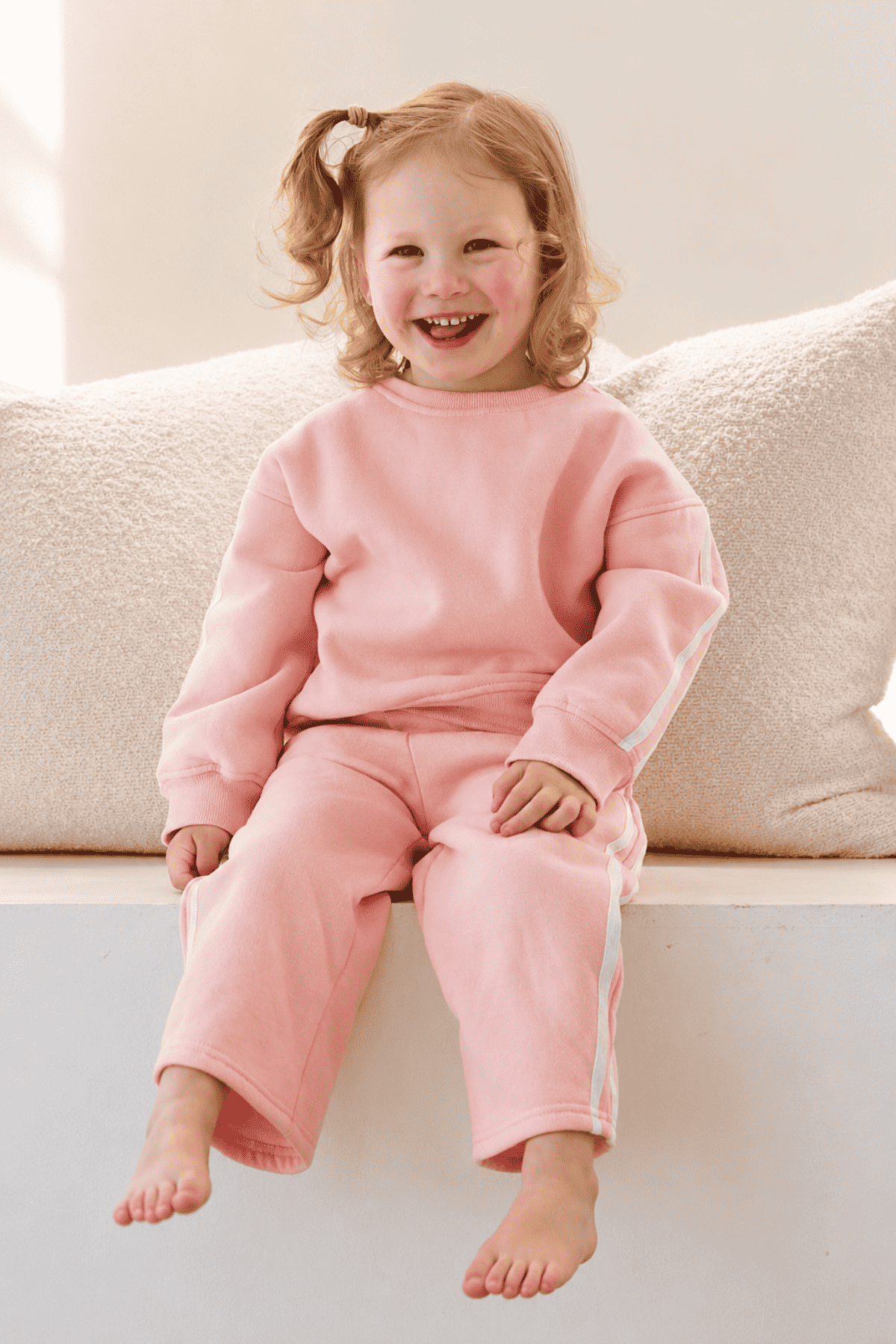 Child wearing pink pajamas sitting on a couch | Elyce is 97cm tall and wears size 3Y.