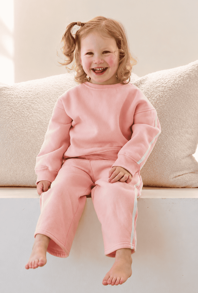 Child wearing pink pajamas sitting on a couch | Elyce is 97cm tall and wears size 3Y.