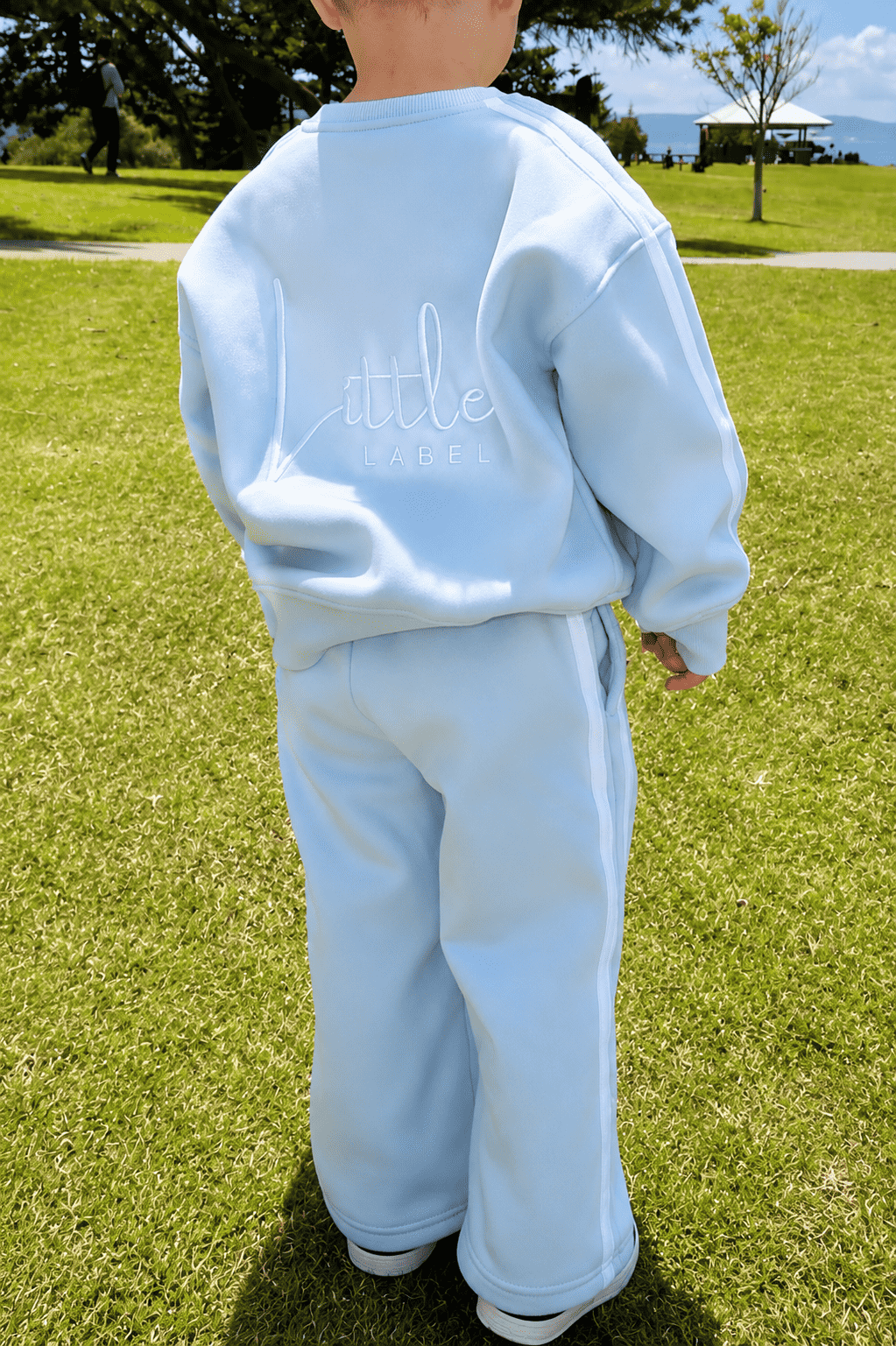 Person wearing a light blue tracksuit with 'Little' text on the back, standing on grass. | Alex is 2'6