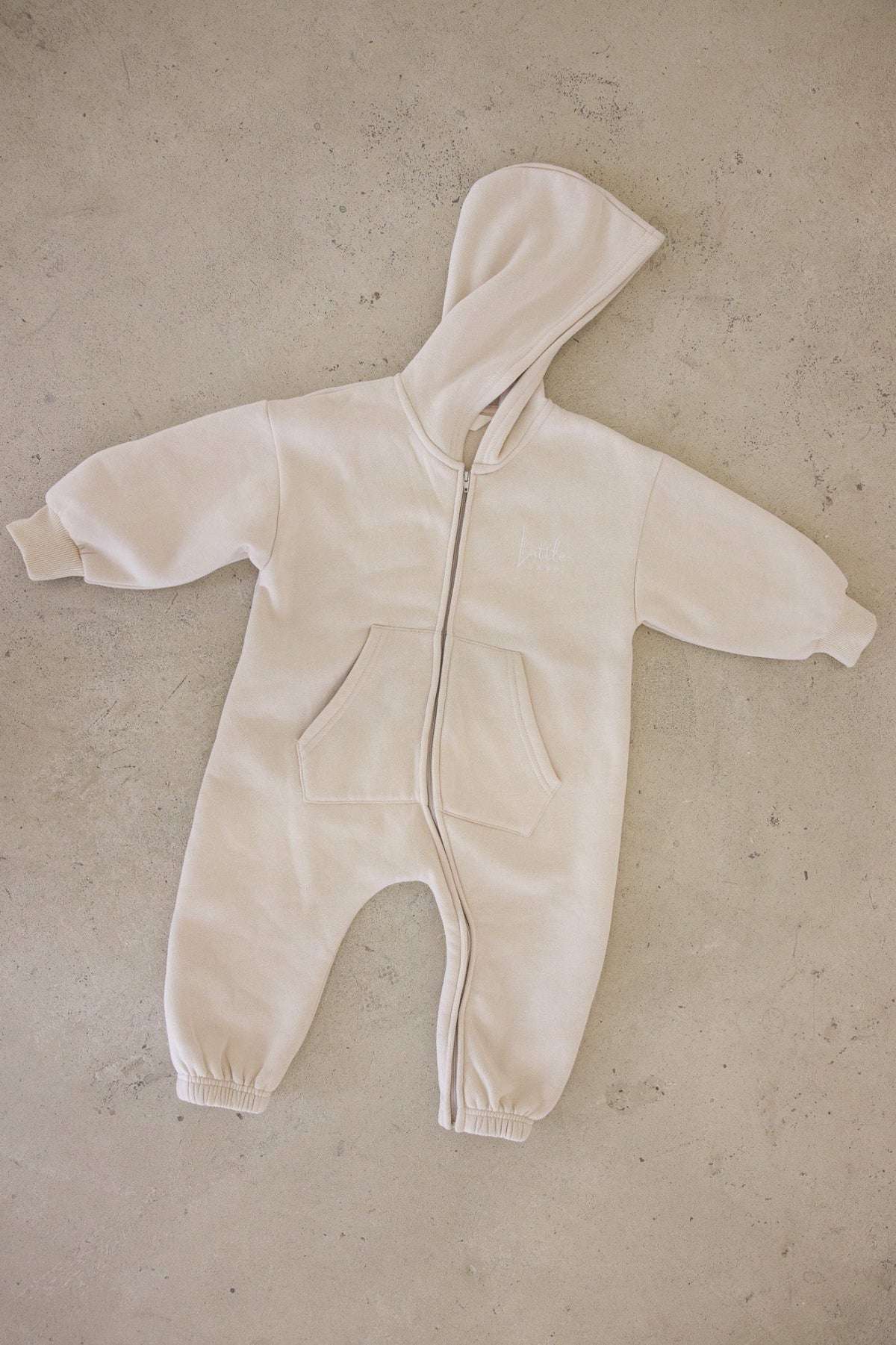 Beige baby onesie with a hood on a beige surface