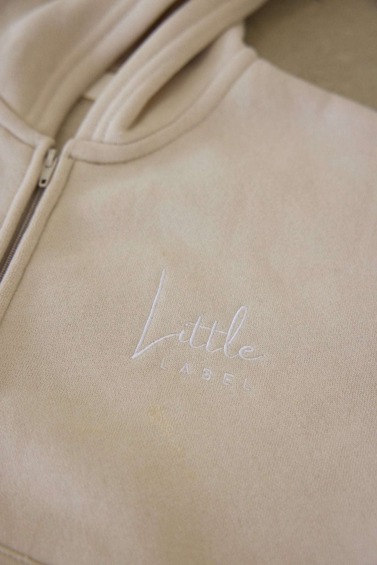Beige hoodie with 'Little Label' embroidery on a beige background