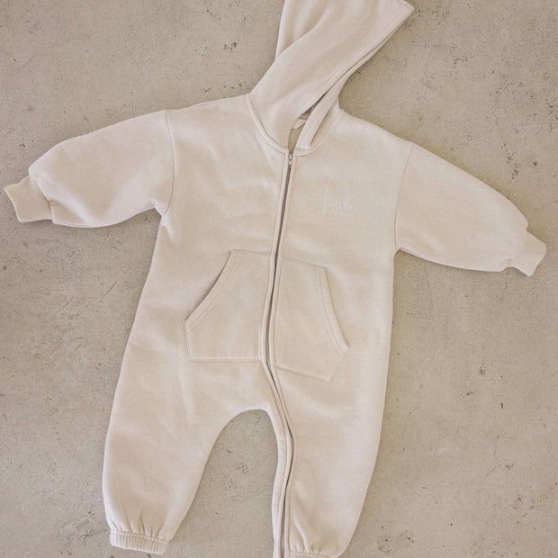 Beige baby onesie with a hood on a beige surface