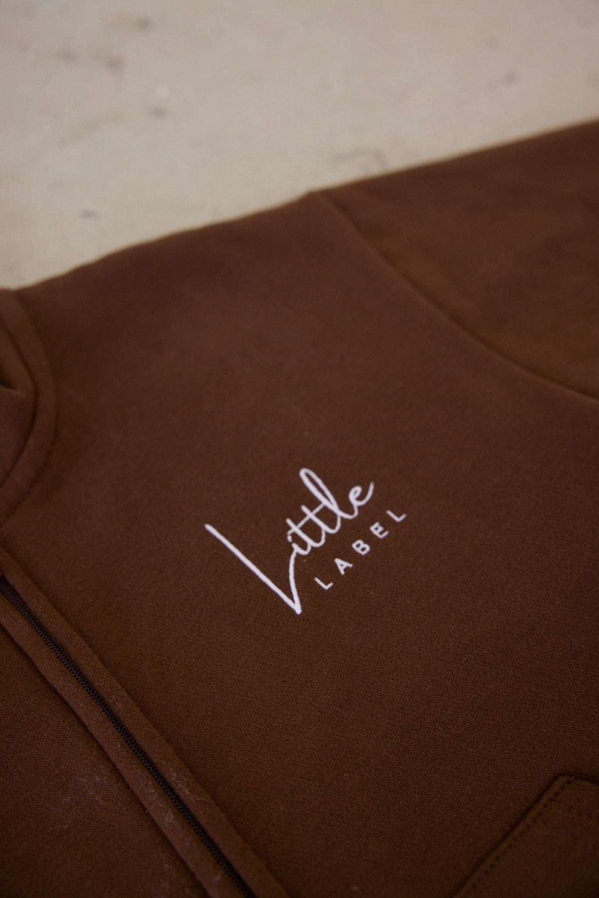 Brown garment with 'Little Label' embroidery on a light background