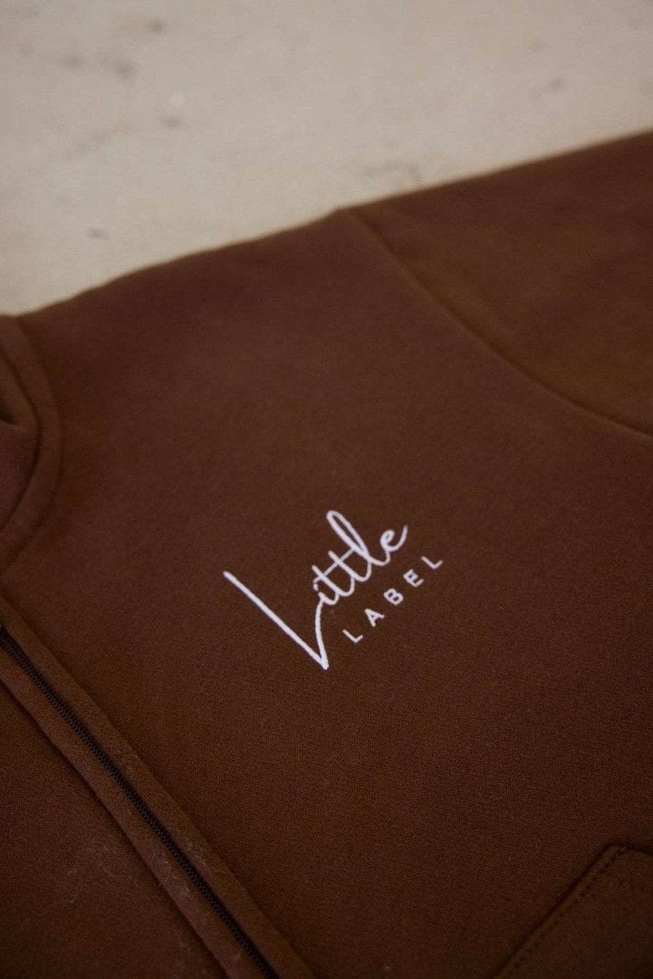 Brown garment with 'Little Label' embroidery on a light background