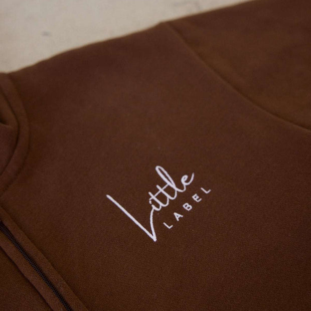 Brown garment with 'Little Label' embroidery on a light background