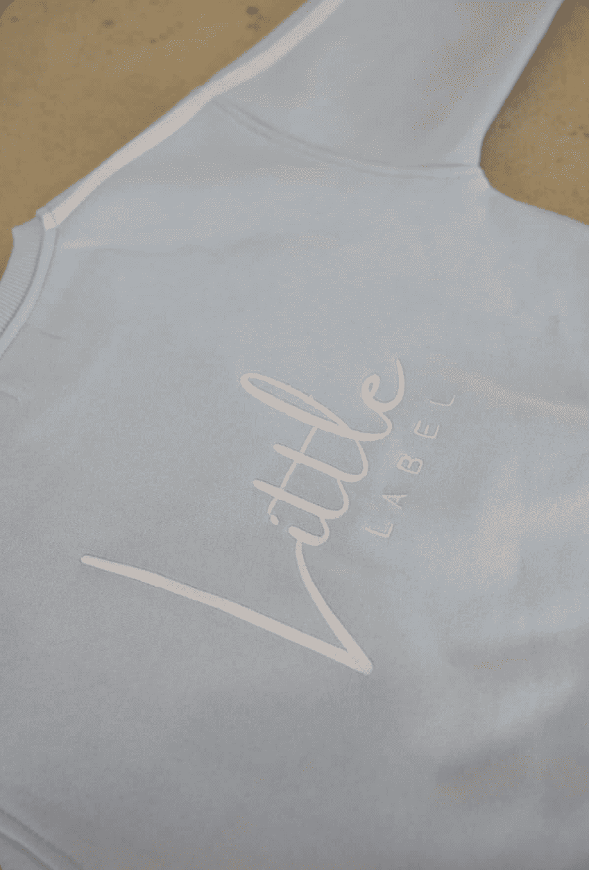 Light blue tank top with 'Little Label' logo on a beige background