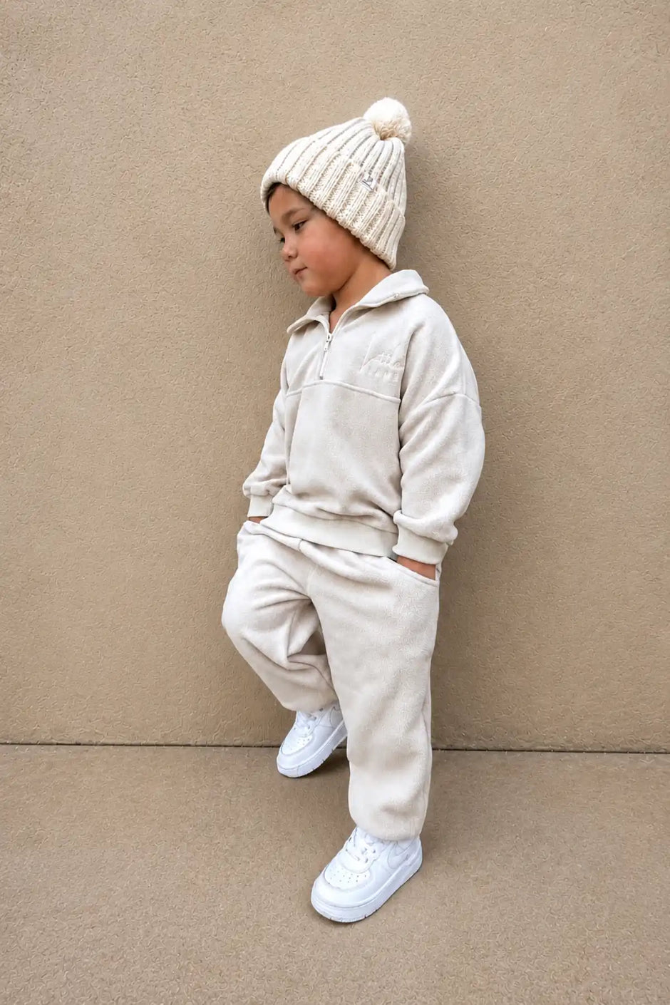 Child wearing a beige fleece outfit with a matching beanie against a beige background