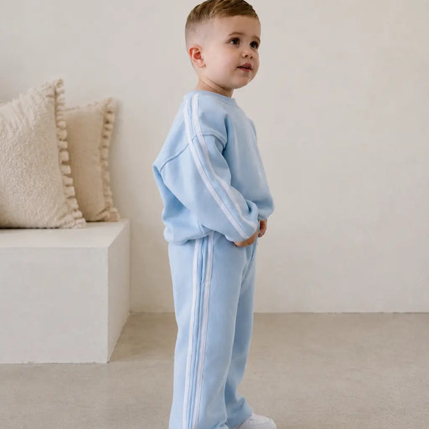 Child wearing a light blue tracksuit standing in a minimalistic room with beige pillows. | Alex is 2'6" (80cm), wears size 2Y.