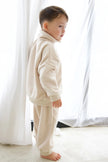 Child wearing a cream-colored outfit standing in front of white curtains. | Ryan is 3'3