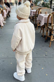 Child in a cream outfit walking on a sidewalk with outdoor seating in the background | Ryan is 3'3