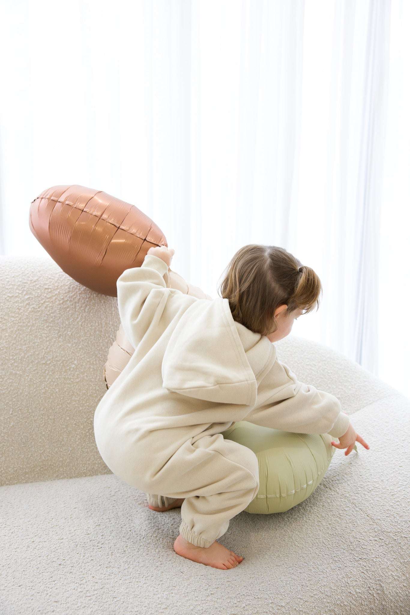Child in a white onesie playing with a football on a light-colored couch | Sophie is 2'7