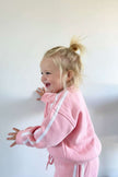 Child in a pink outfit with white stripes on a plain background | Millie is 2'2 (78cm), wears size 2Y