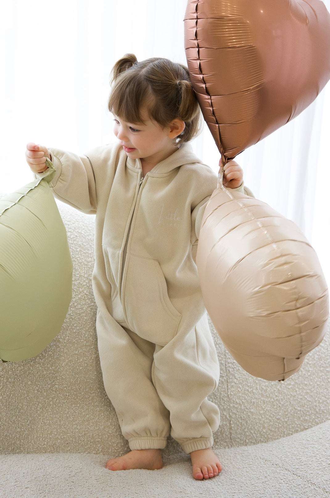 Child in a beige onesie holding balloons on a light-colored carpet | Sophie is 2'7