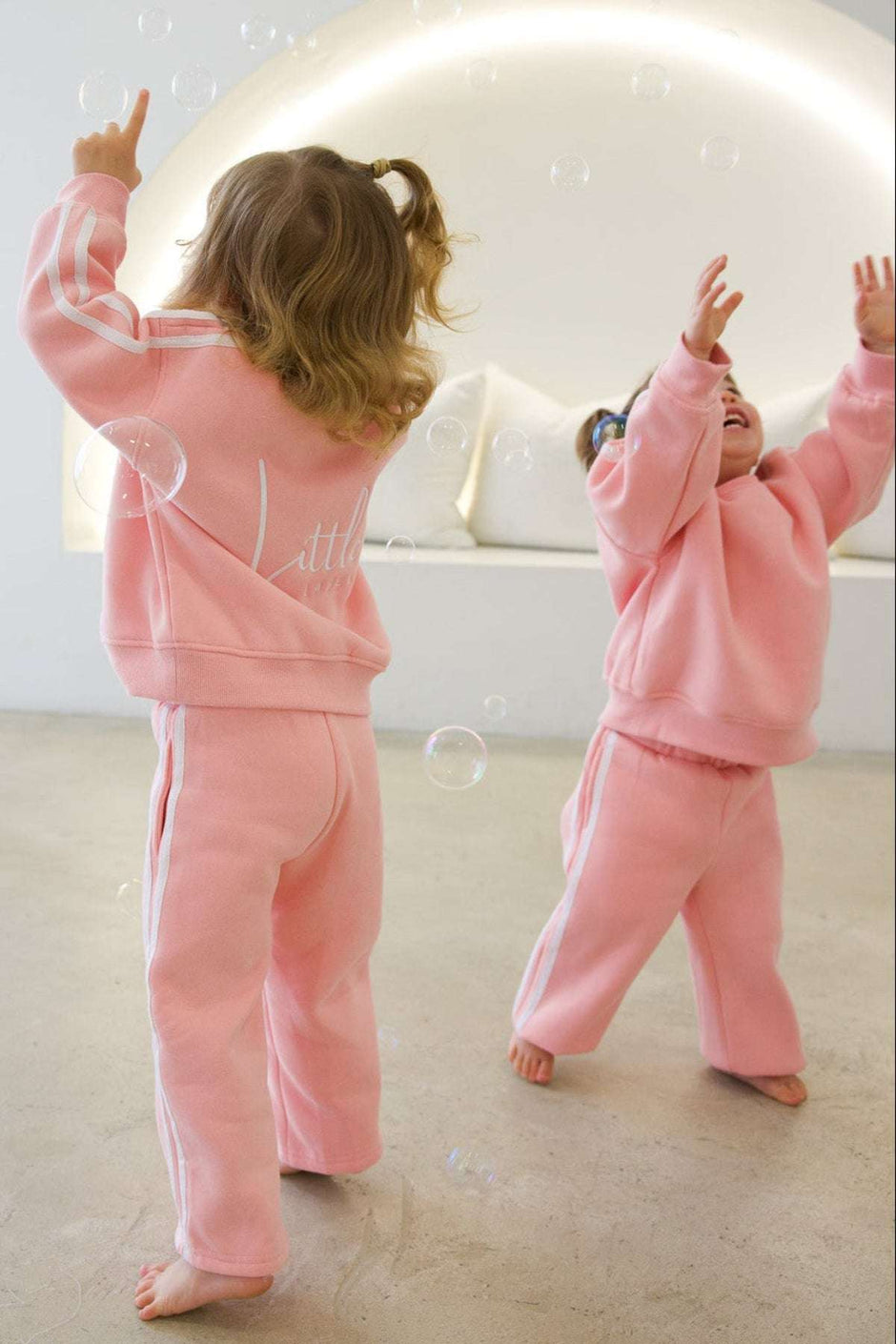 Two children in pink outfits playing with bubbles in a room.