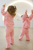 Two children in pink outfits playing with bubbles in a room.