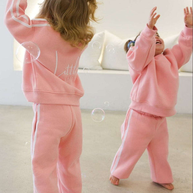 Two children in pink outfits playing with bubbles in a room.